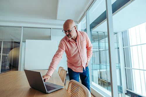 Businessman using laptop in modern office with glass windows and bright natural light