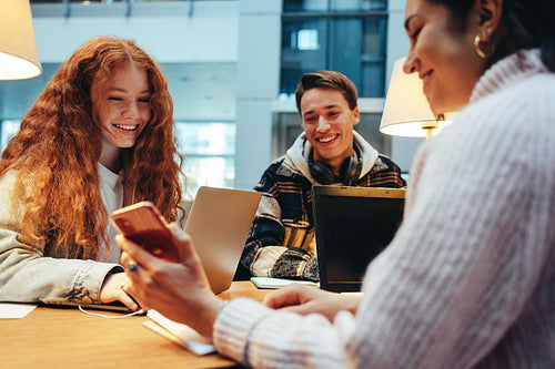 Girl student showing her phone to her friends in library
