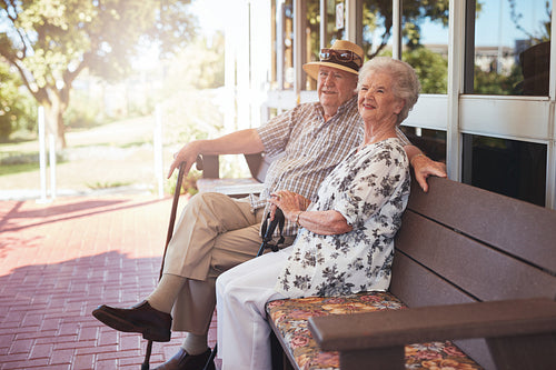 Retired couple sitting on a bench outside their home