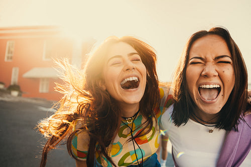 Two friends laughing and posing outdoors enjoying a sunny day