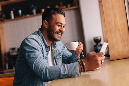 Smiling young man in cafe using mobile phone