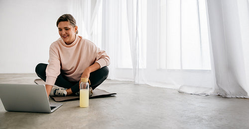 Laptop fitness routine with a woman on a yoga mat at home