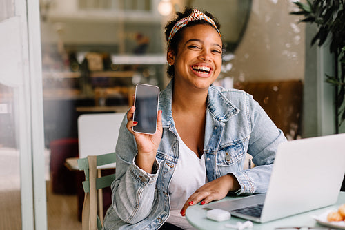 Cheerful woman recommending a mobile app at a coffee shop