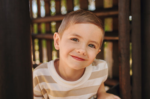 Smiling young boy outdoors under a sunny wooden structure