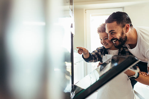 Father and child baking food in an oven at home