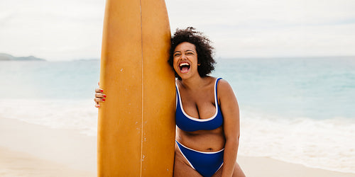 Exciting surfing vacation: Plus size surfer laughing in a bikini at the beach
