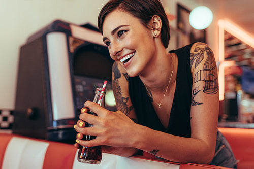 Smiling woman holding a soft drink bottle standing at a restaurant