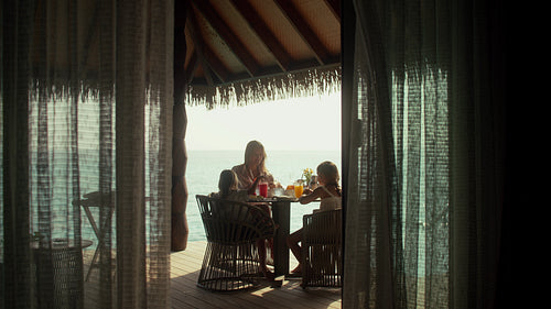 Family enjoying breakfast on a tropical island resort overwater villa deck during their vacation