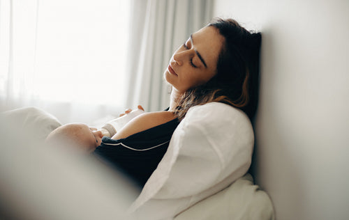 Mother soothing baby while feeding and resting in bed