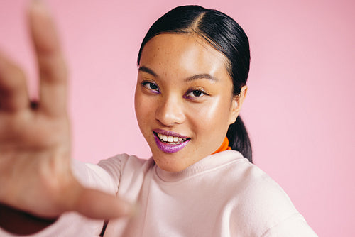 Youthful woman in her 20s blocks the camera with her hand in a studio