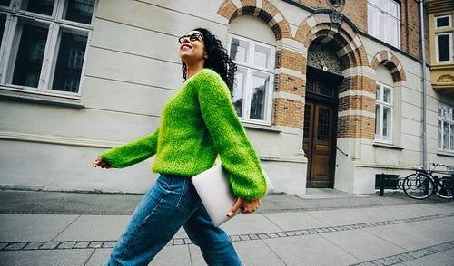 Woman walking confidently with laptop in city for work and success