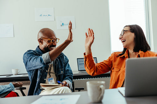 Co-workers celebrating success with a high-five in a modern office setting