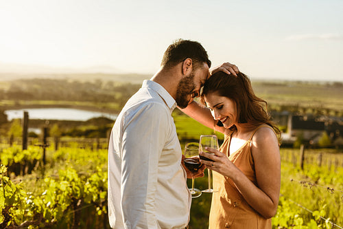 Couple in love standing in a vineyard holding wine