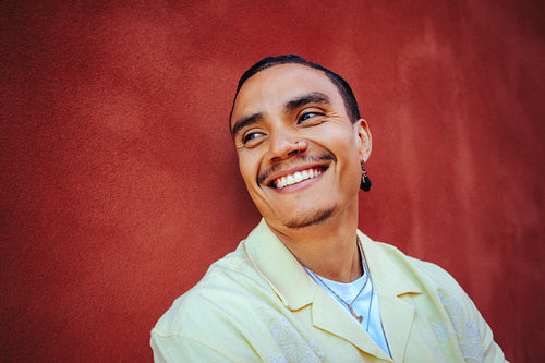 Smiling man leans by a red wall in an urban outdoor portrait