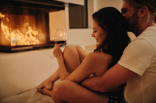 Romantic couple enjoying wine by fireplace in cozy setting