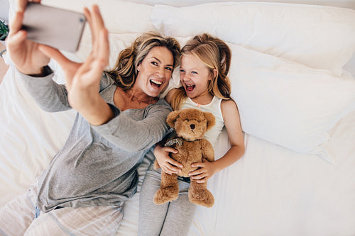 Young mother taking selfie with her daughter on bed
