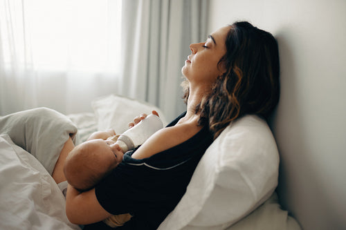 Tired mother feeding baby with bottle
