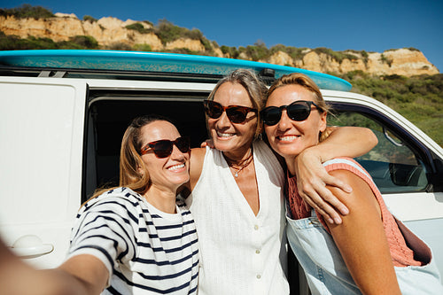 Friends smiling for a selfie during a surfing vacation near a camper van