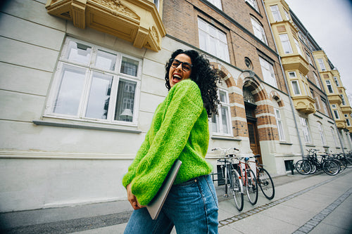 Young woman happily walking through city with laptop