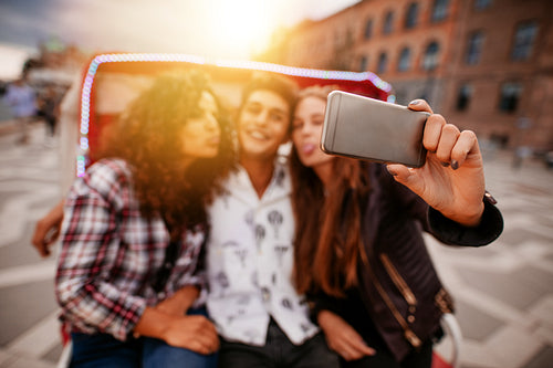 Young woman taking selfie on tricycle with friends