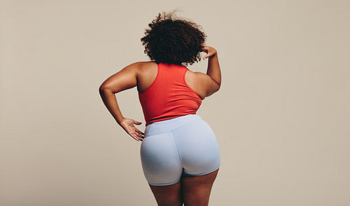 Rearview of a body confident woman standing in a studio, wearing sportswear