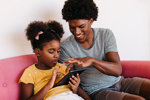 Gen Z siblings relaxing together on sofa, using digital tablet