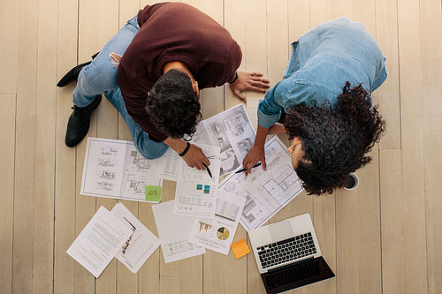 Business colleagues sitting on the floor and discussing work with business papers spread on the floor