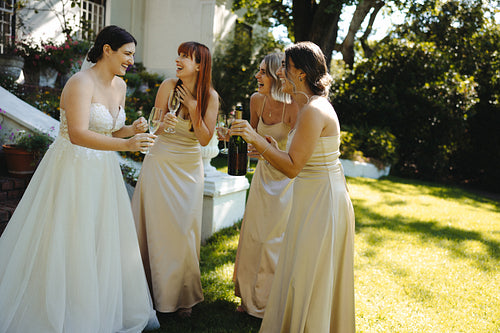 Bride and bridesmaids laughing with champagne at outdoor wedding