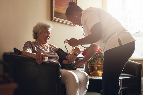 Nurse measuring blood pressure of senior patient in retirement home
