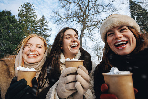 Women drink hot chocolate together outdoors in winter