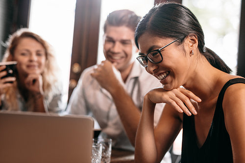 Smiling woman looking at laptop with friends in cafe