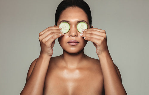 Beautiful woman holding cucumber over eyes