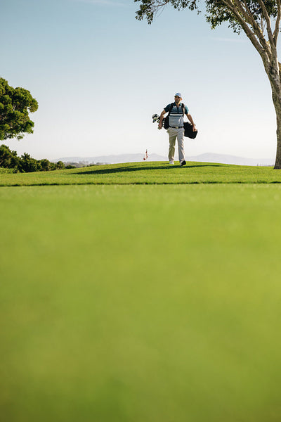 Wide angle of male golfer walking on towards the green holding golf clubs on a sunny day