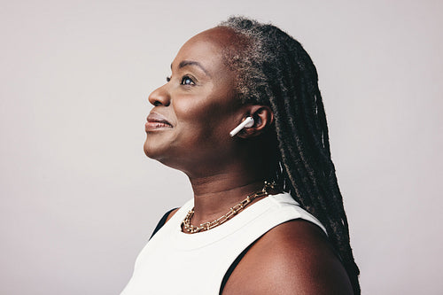 Mature woman with dreadlocks listening to music on wireless earbuds