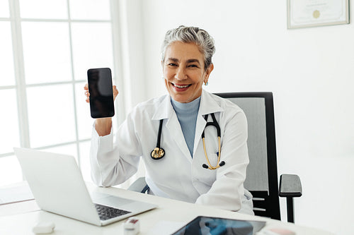 Recommended by a doctor: Happy senior doctor holding up a smartphone and smiling at the camera