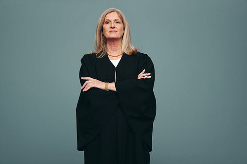 Mature judge standing with her arms crossed in a studio