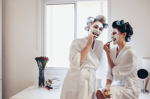 Smiling mother and daughter eating slices of cucumber with face pack on