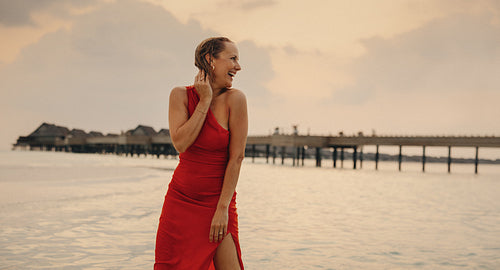 Elegant sunset serenity: Mature woman in red gown radiating vitality on tropical island beach