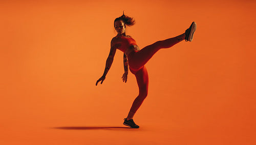 Fit woman doing leg stretches on orange background