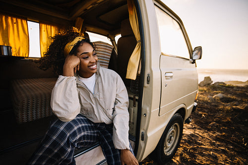 A woman relaxing in a camper van listening to the ocean at sunset