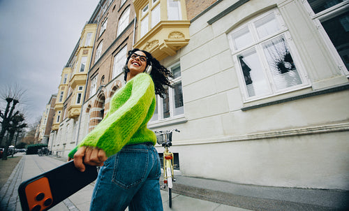 Her woman-on-the-go style shows as she carries a skateboard and streams music in the city