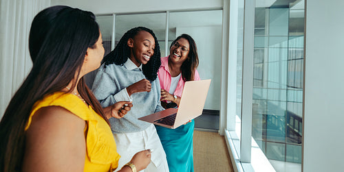 Multicultural team of joyful coworkers sharing a laugh over a laptop in a bright office setting