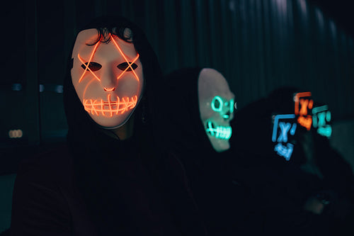 Individuals wearing neon-lit masks in a dark atmospheric urban setting