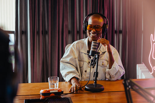 Happy podcaster speaking into microphone in studio with neon lighting