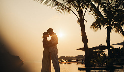 Romantic couple embracing at sunset silhouette during vacation on tropical beach