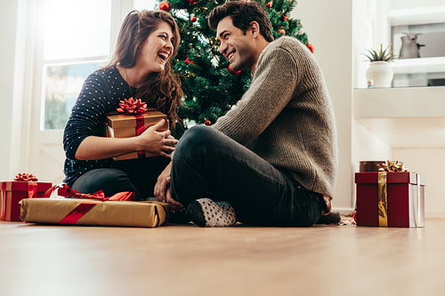 Young couple exchanging Christmas gifts at home.