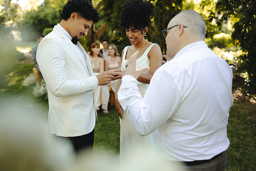 Bride and groom exchanging rings during outdoor wedding ceremony on sunny day