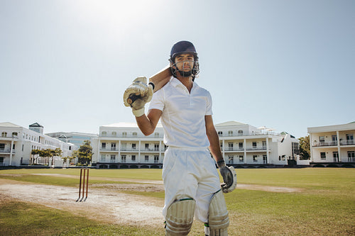 Male cricket player standing on a field holding a bat
