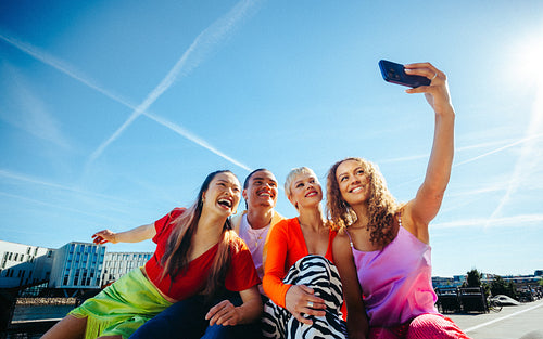 Friends capture a selfie with a smartphone outdoors beneath a blue sky