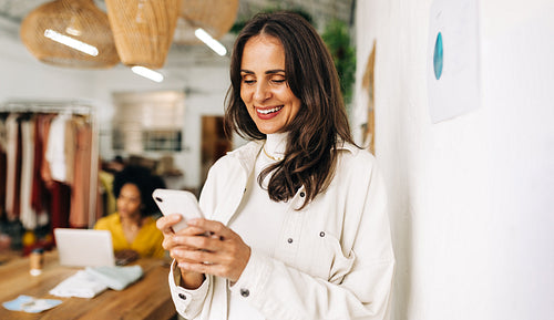 Happy designer reading a text message on a smartphone in a clothing store